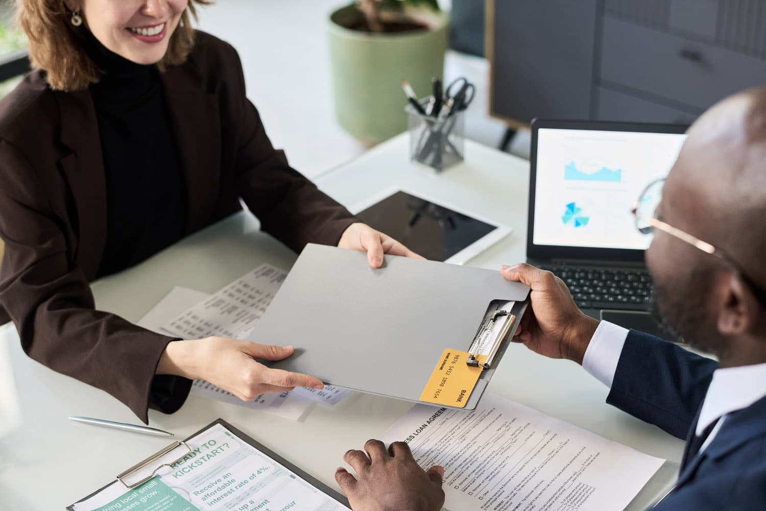 Board member passing a clipboard of financial documents across a table to an auditor