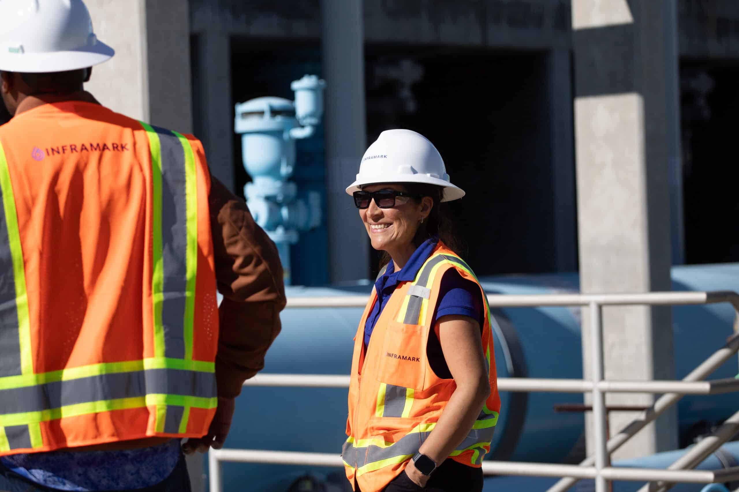Two Inframark employees wearing orange safety vests and hard hats on-site