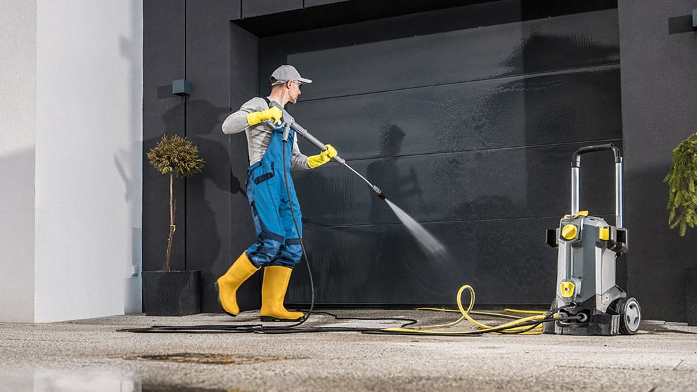 maintenance worker cleaning garage door with pressure washer