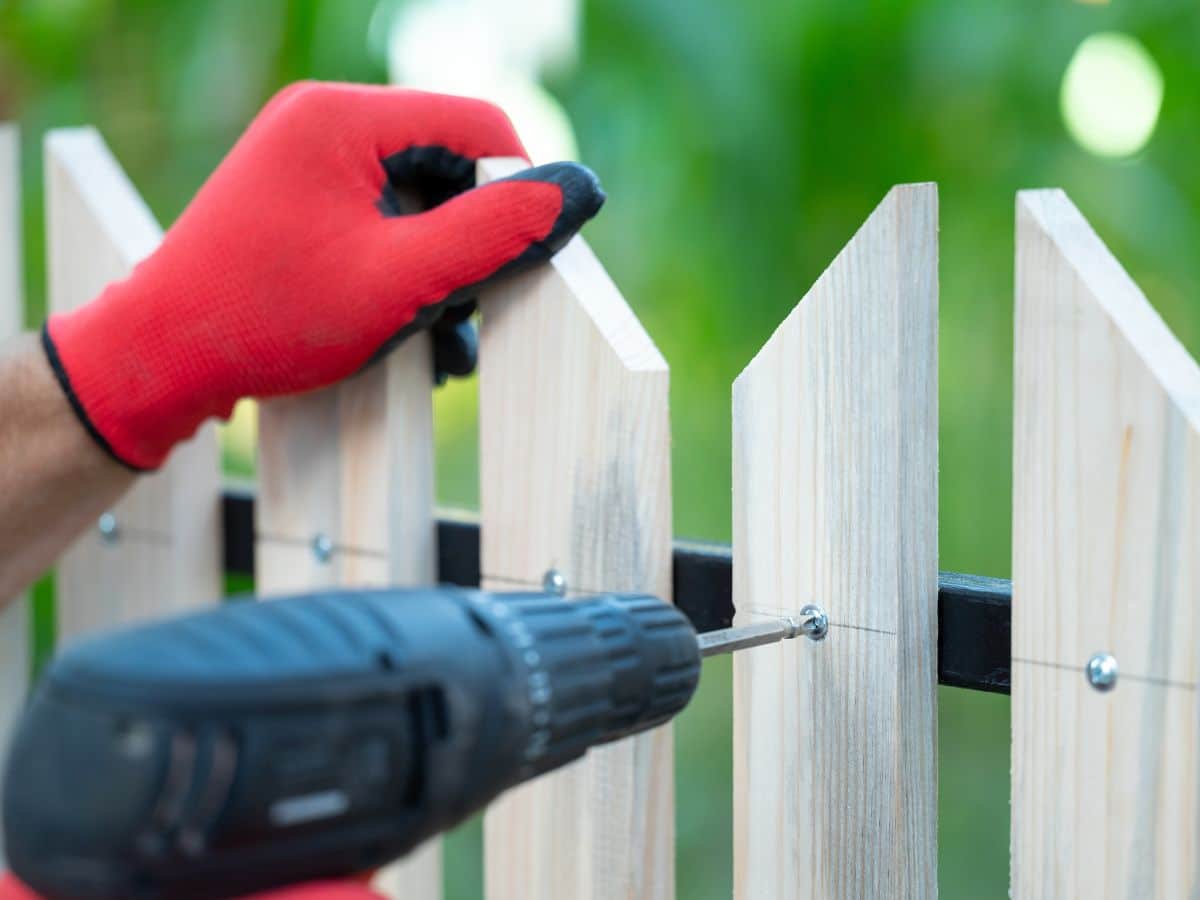 maintenance worker repairing white picket fence