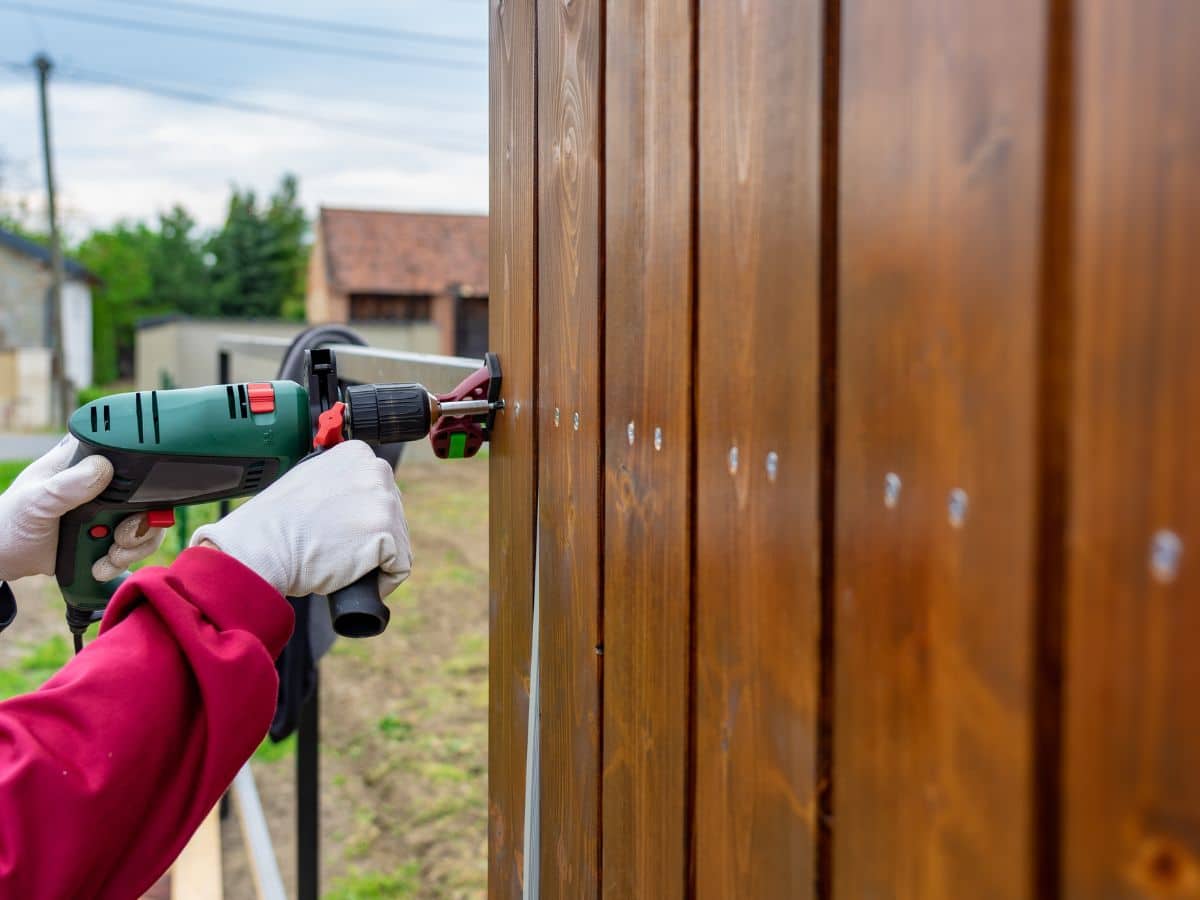 male maintenance worker using drill to repair wooden fence