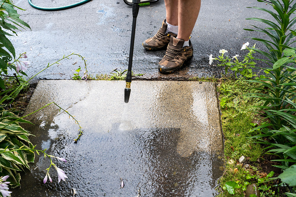 man pressure washing house pathway